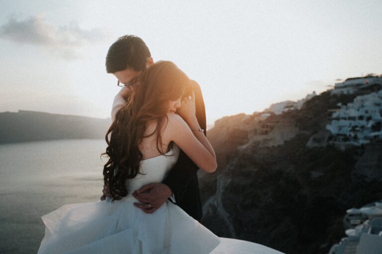 Hun holds Irene in her wedding gown on a clifftop in Santorini at sunset