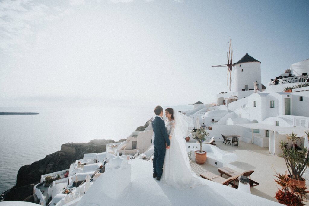 Felicia and Andrew on a white terrace in Santorini, with a windmill and the sea