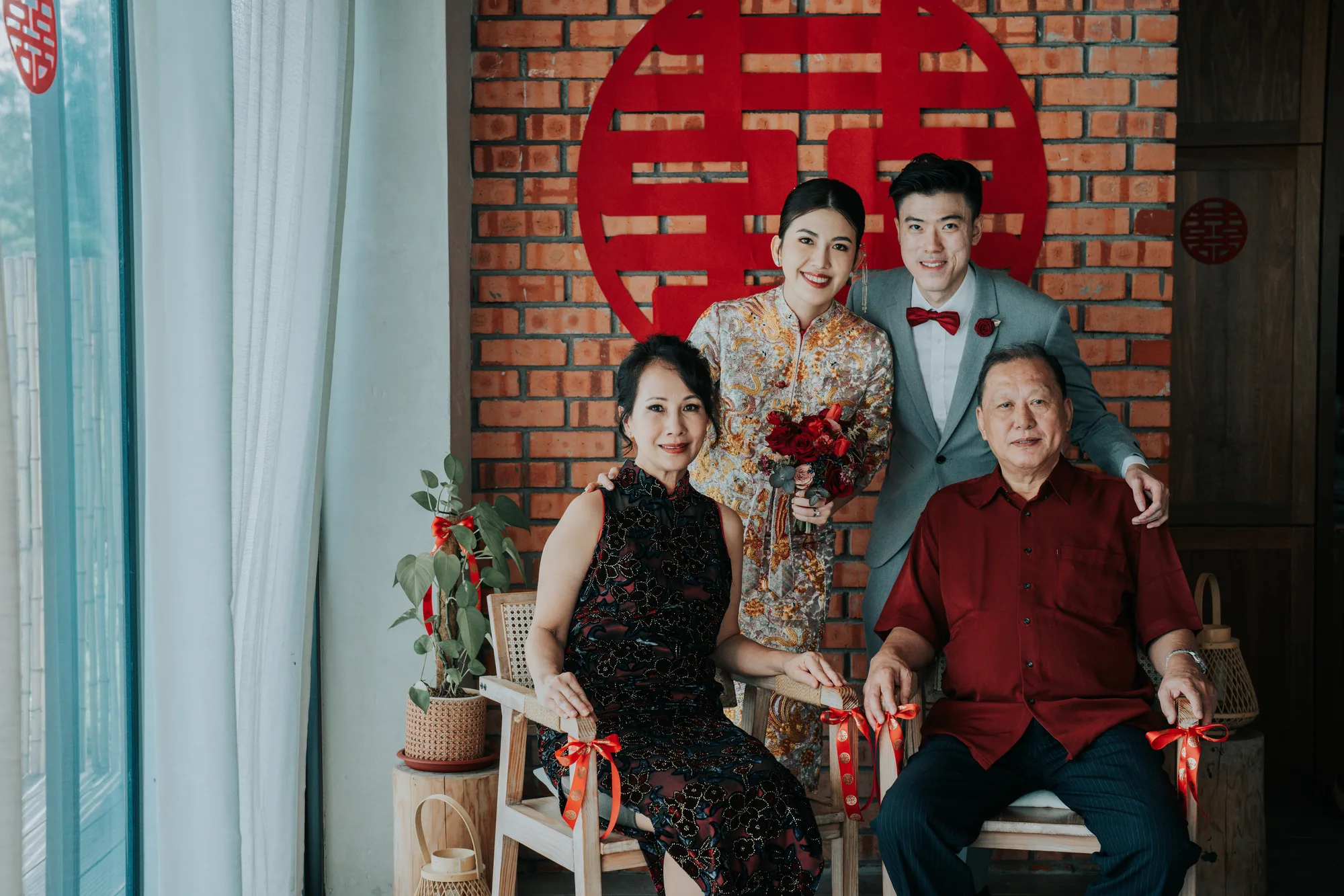 A family poses in front of a brick wall with a red double happiness symbol