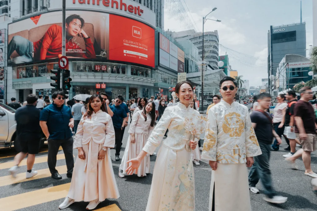A newlywed couple in traditional attire walks through a bustling urban street during the day