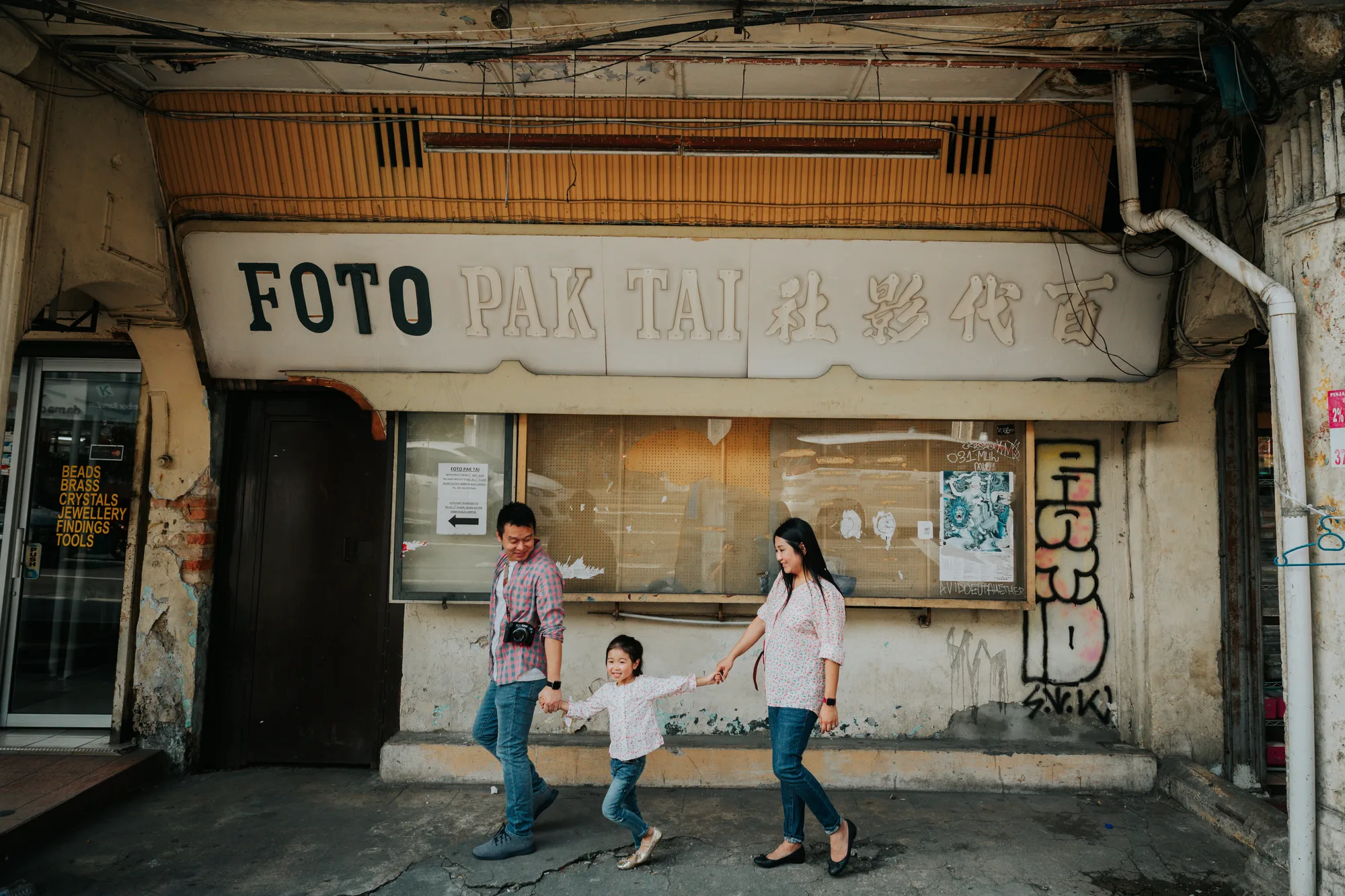 A family of three walks hand in hand past an old photo studio shopfront