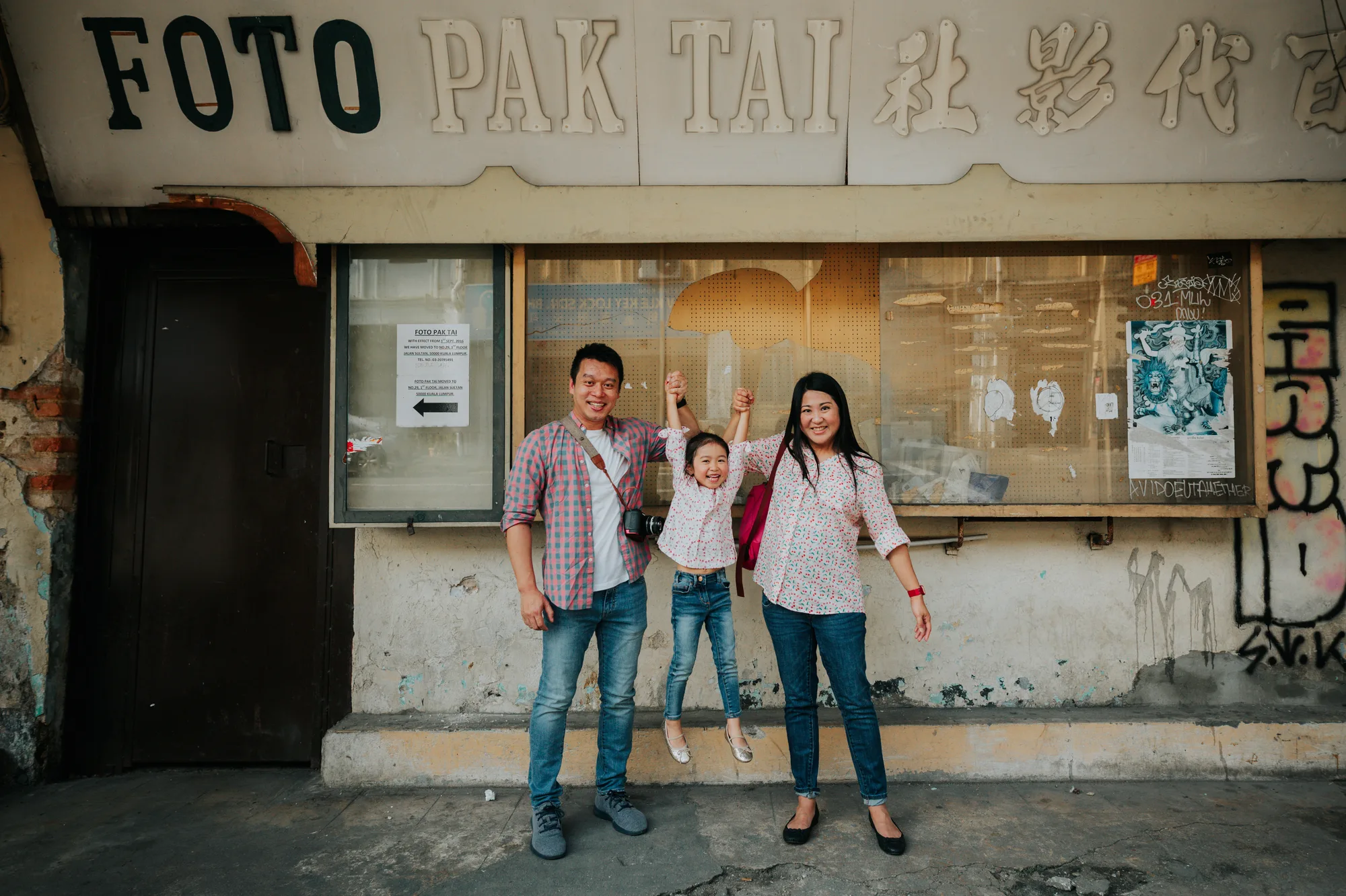 A family of three stands in front of an old photo studio shopfront with its painted sign