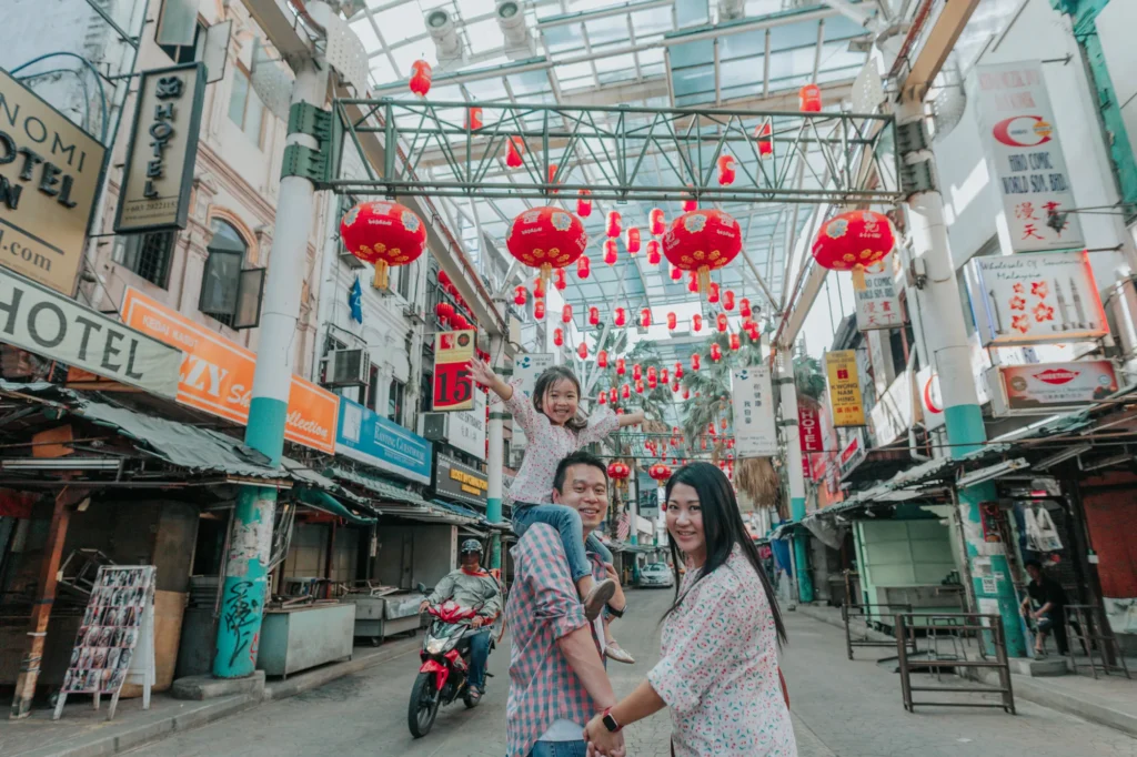 A family of three enjoys a playful moment in an urban alleyway adorned with red lanterns