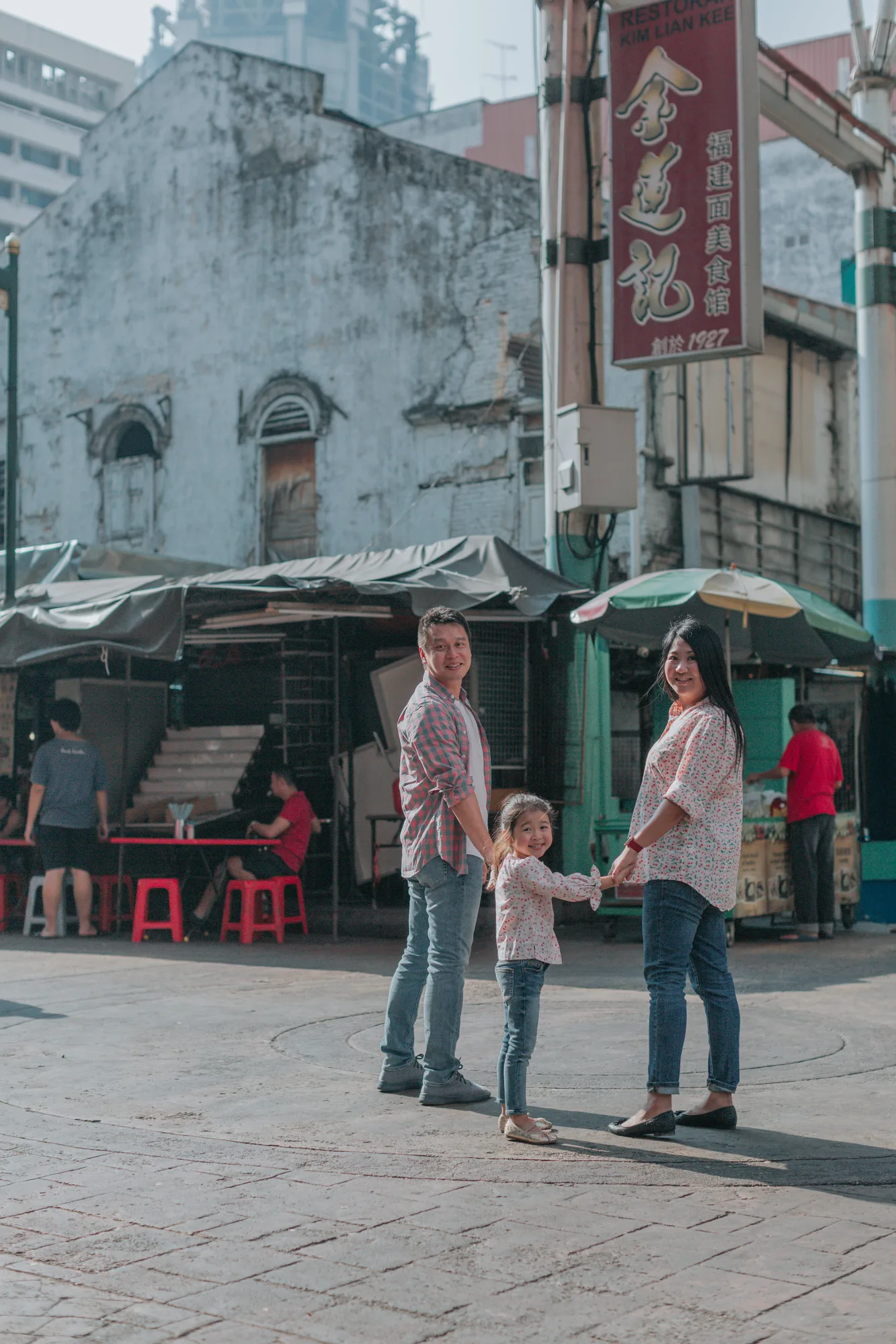 A family of three stands together in a sunny street market