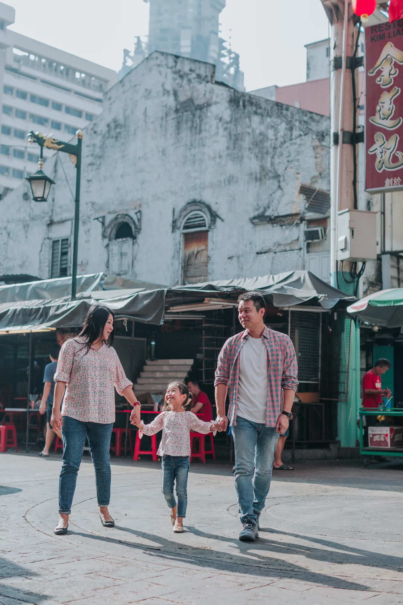 A family of three walks together past old shophouses and market stalls