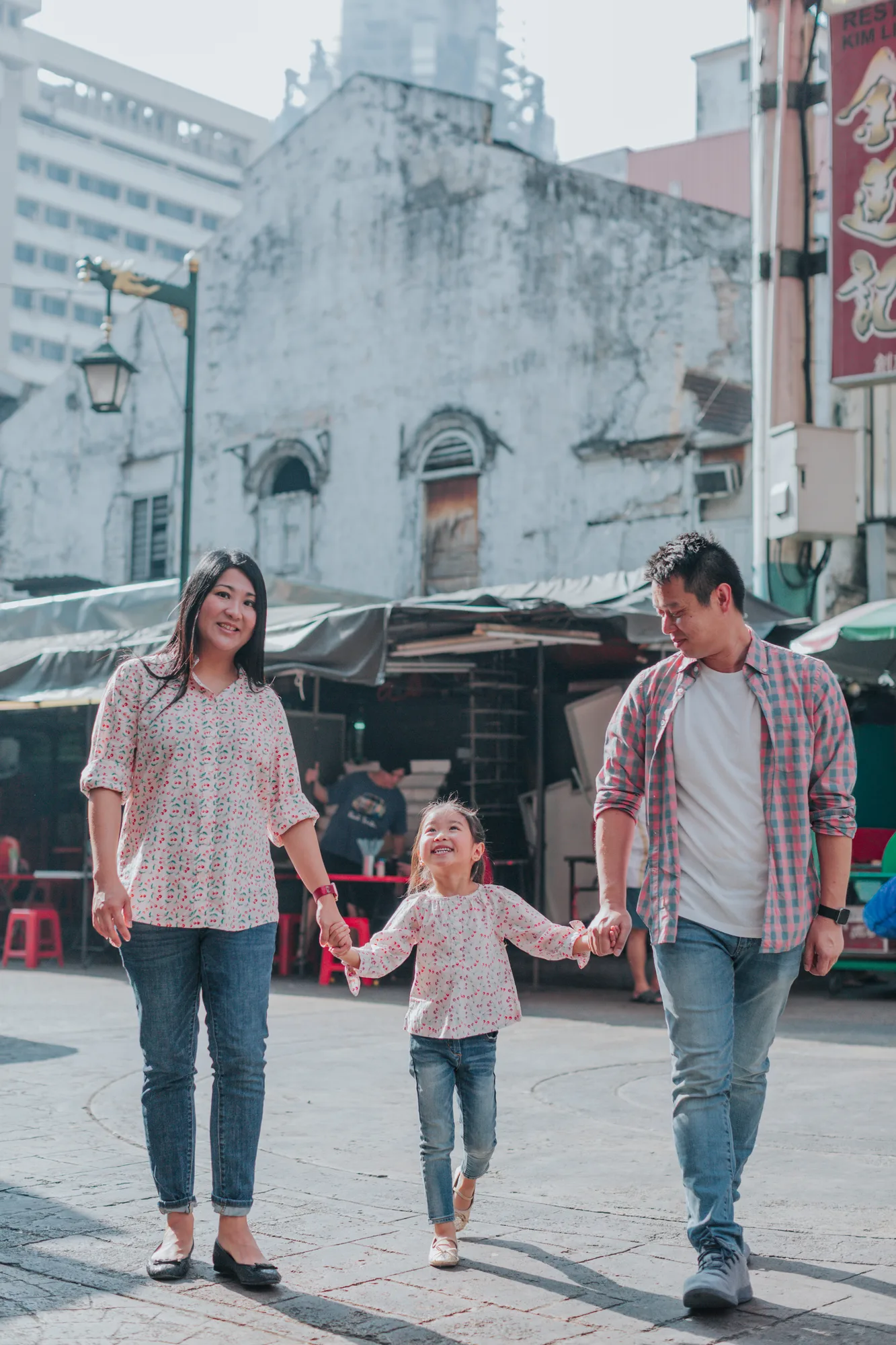 A family of three walks hand in hand through an old market square