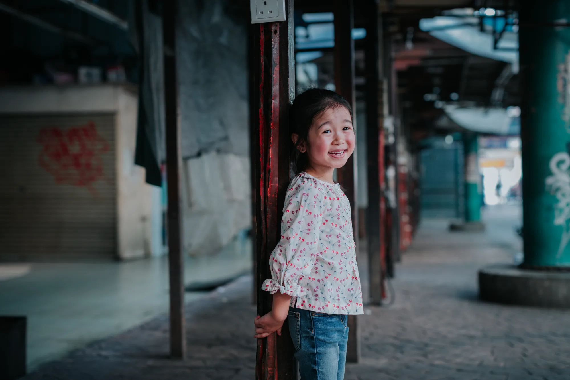 A young girl smiles in a quiet alleyway with graffiti on the pillars