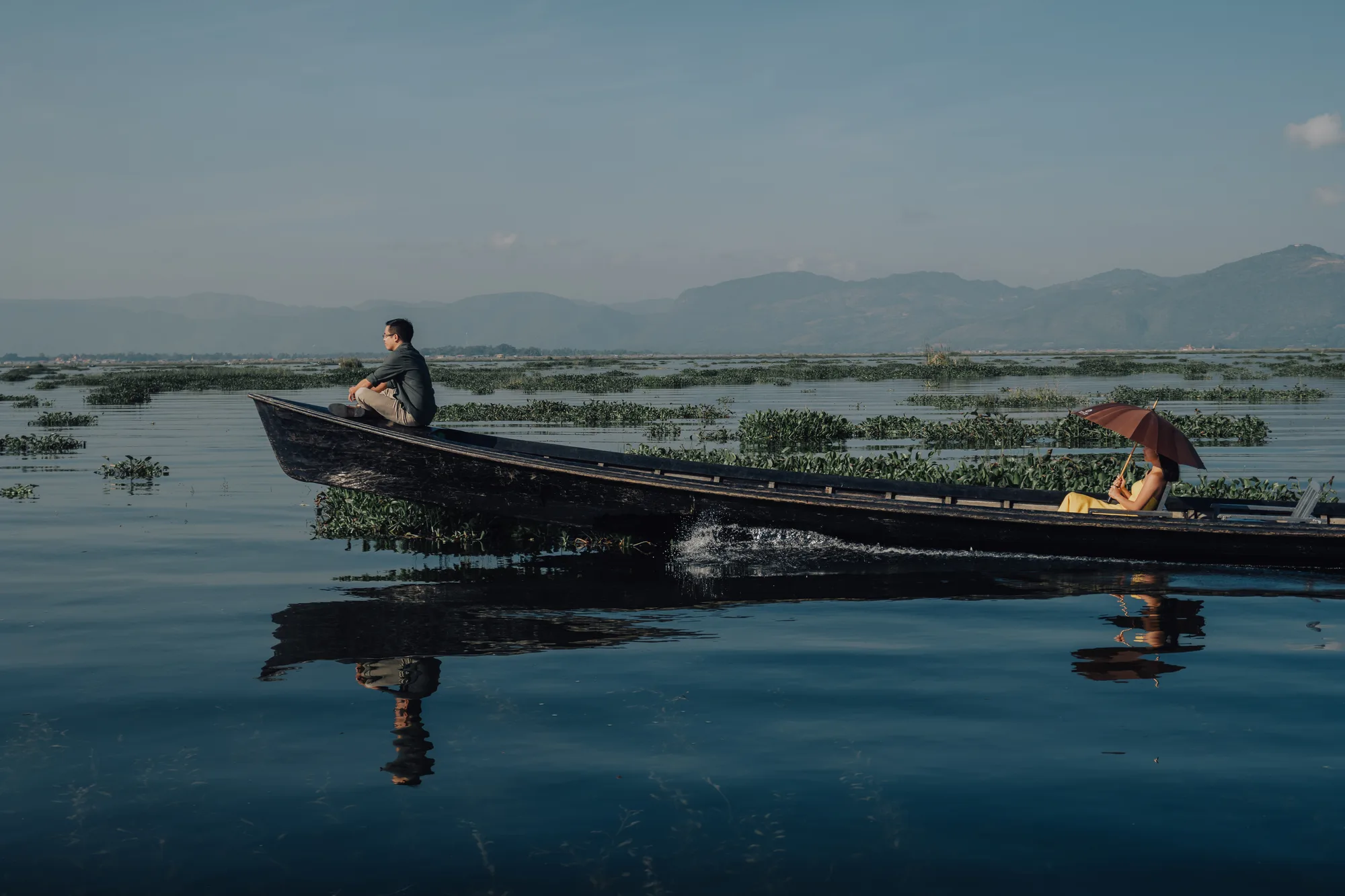 Two people in a boat on a serene lake with mountains in the background