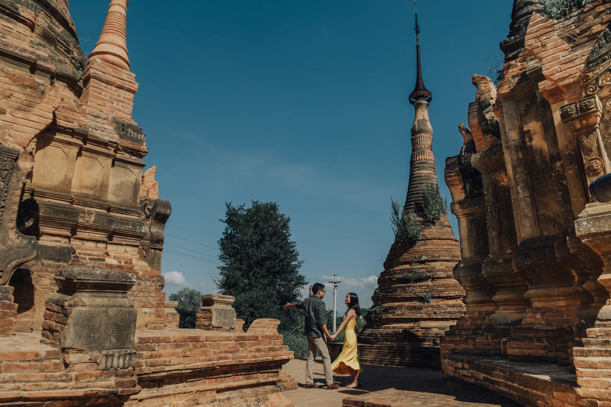 A couple holds hands amidst ancient temples under a clear blue sky