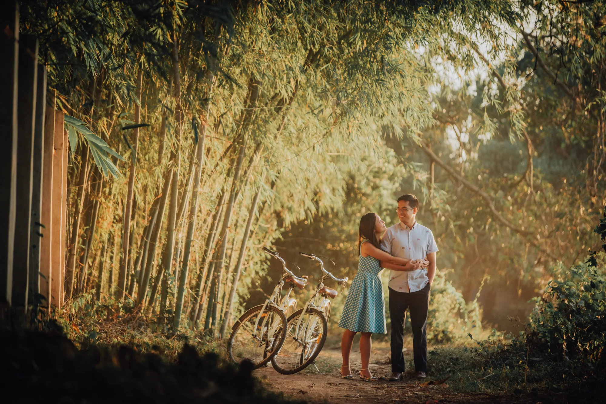 A couple stands together in a bamboo grove with bicycles nearby