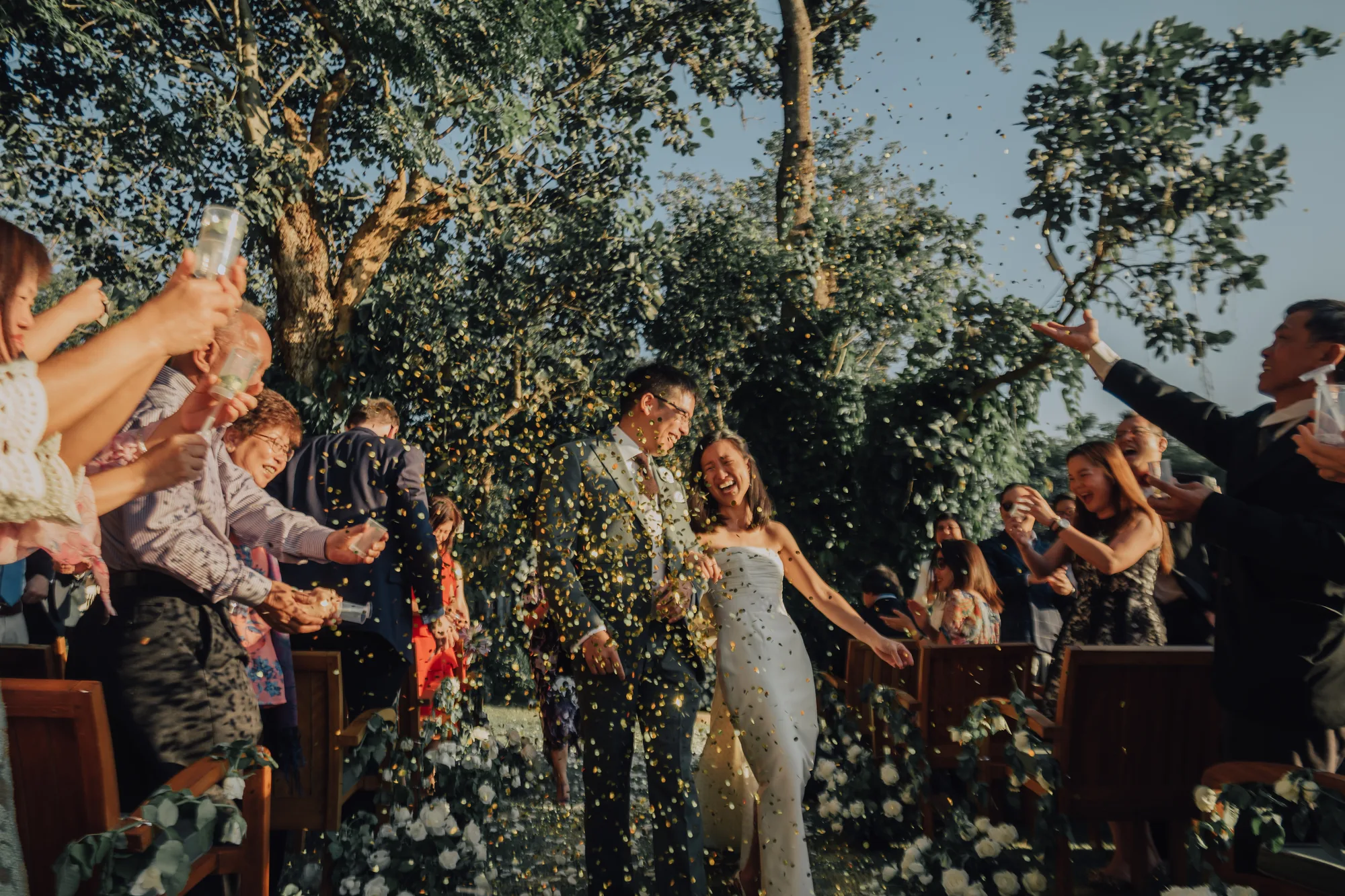A bride and groom laughing as guests throw confetti over them down the aisle at their Inle Lake wedding