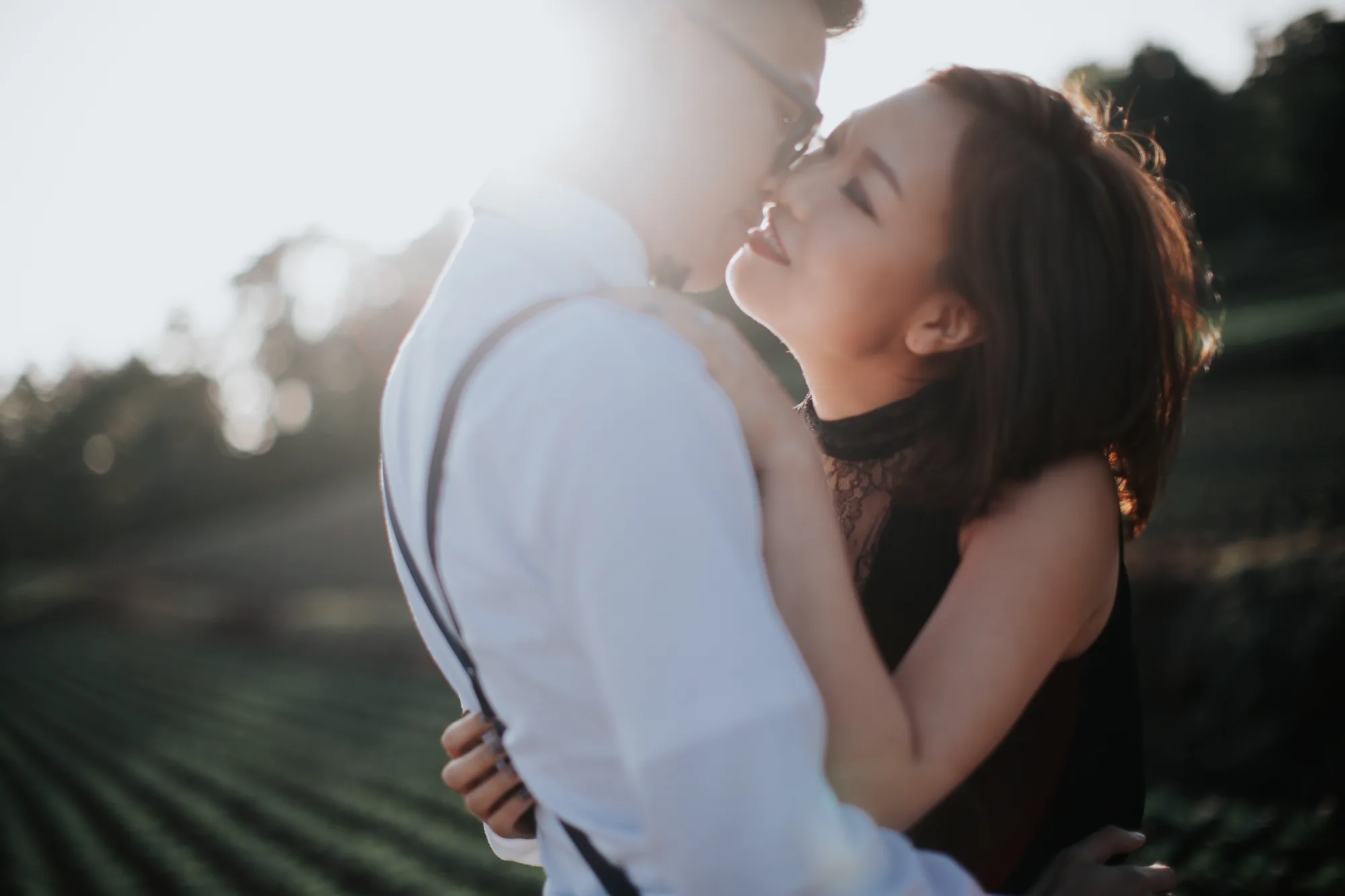 A couple embraces tenderly in a sunlit field at sunset.