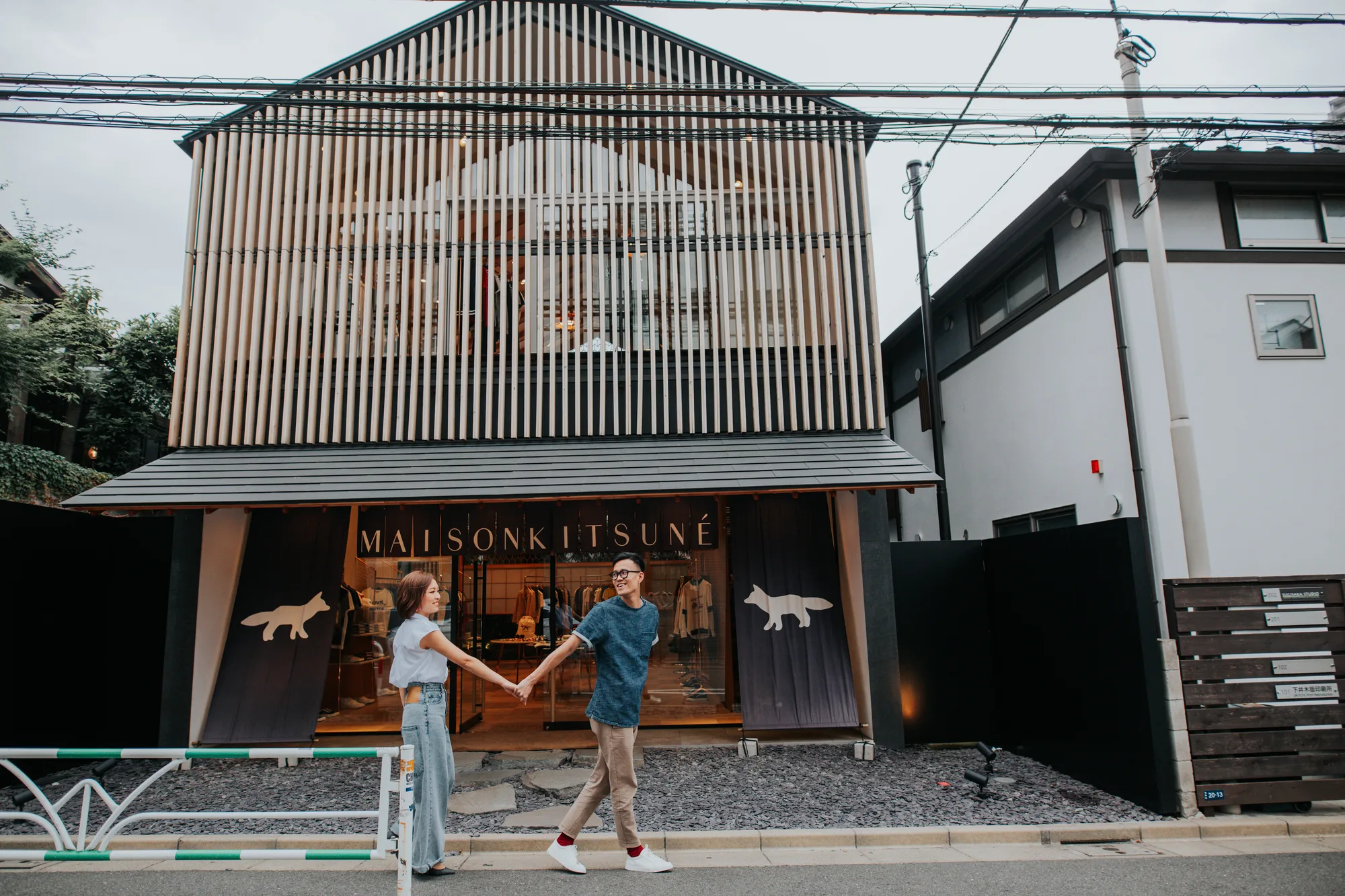 A couple holds hands in front of a Maison Kitsuné store on a cloudy day