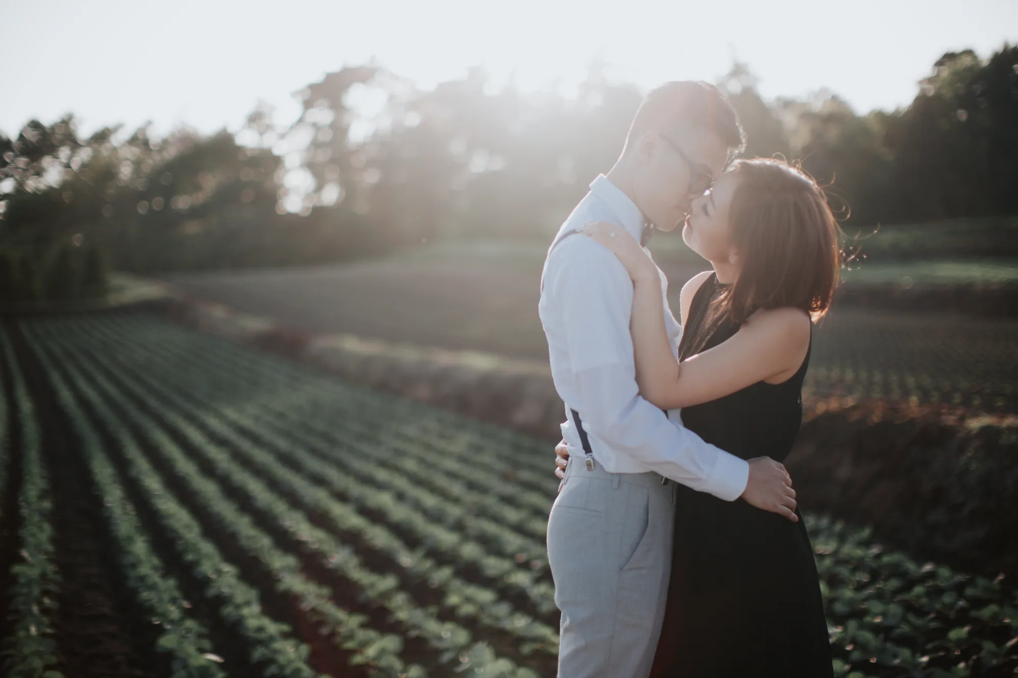 A couple shares a tender moment in a serene field at sunset