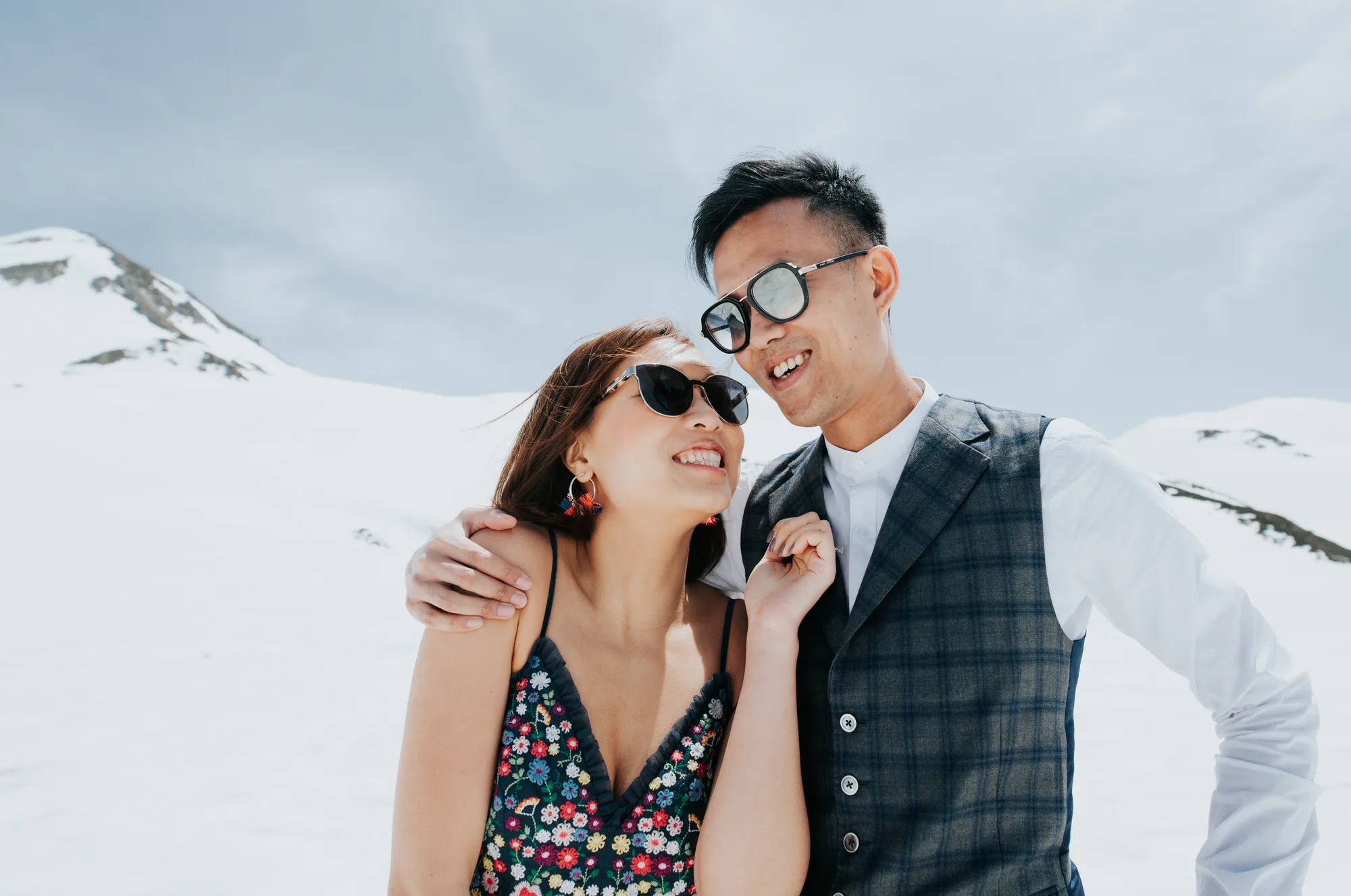 A couple enjoys a snowy mountain backdrop under bright sunlight