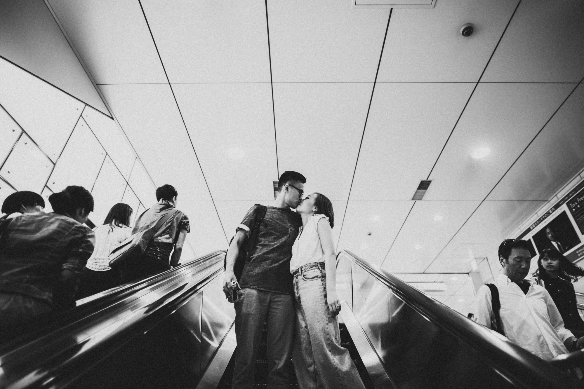 A couple shares a kiss on an escalator amidst other travelers