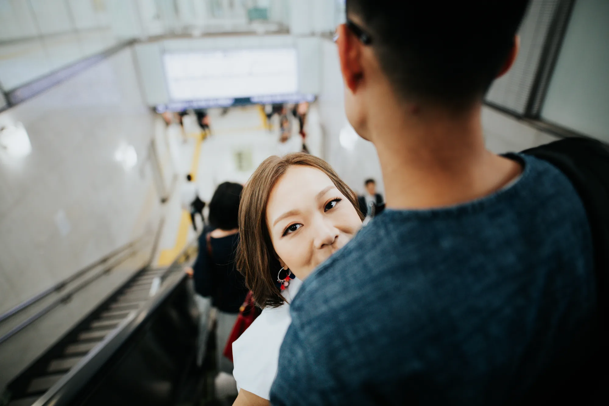 A couple is seen on an escalator in a modern urban setting under artificial lighting
